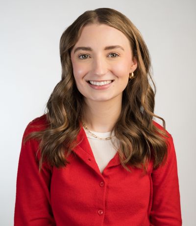 Nicole Jasperson A smiling woman with long, wavy brown hair, wearing a red cardigan over a white top and a gold chain necklace, identified as Nicole Jasperson, Digital Marketing Specialist. Her favorite product is Dreamsicle Sno.
