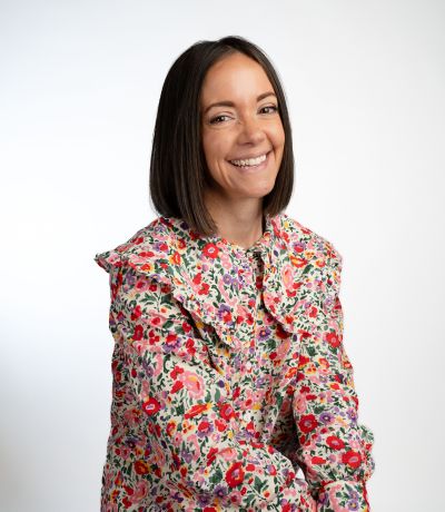 Caroline Petty A smiling woman with short, dark hair, wearing a floral-patterned blouse with a ruffled collar, identified as Caroline Petty, Brand Development Manager. Her favorite product is Unicorn Sno.