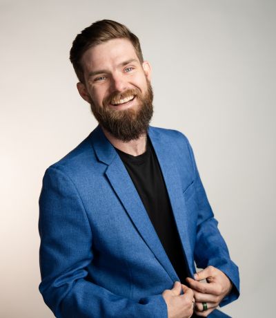 Kolten Knox A smiling man with a beard and short brown hair, wearing a blue suit jacket over a black t-shirt, identified as Kolten Knox, Video Production Manager. His favorite product is Jamaican Punch Sno.