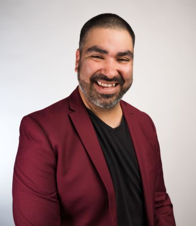 Jacinto Sanchez A smiling man with short dark hair and a beard, wearing a maroon blazer over a black t-shirt, identified as Jacinto Sanchez, Production Manager. His favorite product is Cherry Coke BRM with Vanilla Ice Cream.