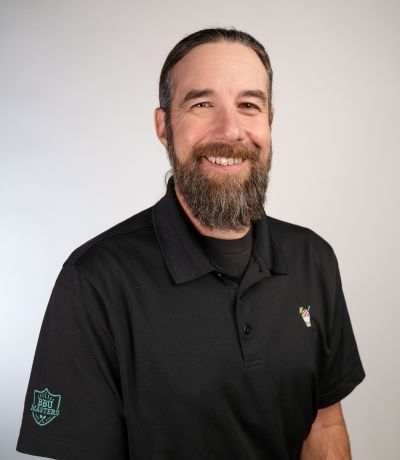 Kyle Bradley A smiling man with long dark hair tied back and a full beard, wearing a black polo shirt with a colorful logo and a "BBU Builders" emblem on the sleeve, identified as Kyle Bradley, Director of Project Development. His favorite product is Wavebender Smoothie