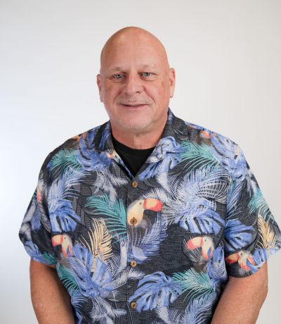 Todd Thompson A smiling man with a bald head wears a short-sleeved Hawaiian-style shirt with blue, green, and orange tropical patterns and toucans, identified as Todd Thompson, Franchise Development Consultant. His favorite product is Toasted Coconut BRM with Chocolate Creme.