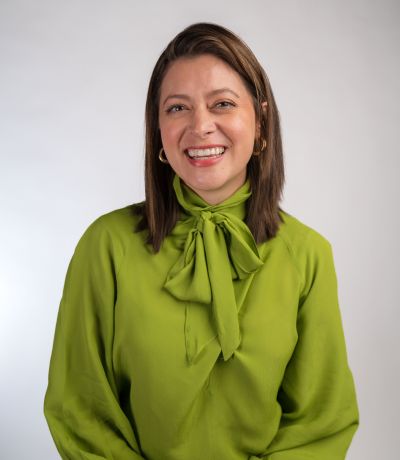 Allison Davis A smiling woman with shoulder-length dark hair and gold hoop earrings wears a bright lime green blouse with a necktie detail, identified as Allison Davis, Internal Operations Manager. Her favorite product is Mango Sno with Chili Salt
