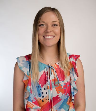 Steffanie Appleton A smiling woman with long, blonde hair wears a colorful sleeveless top with a blue, pink, red, and orange abstract pattern, identified as Steffanie Appleton, Internal Operations Specialist. Her favorite product is Piña Colada Sno with Tropic Creme.