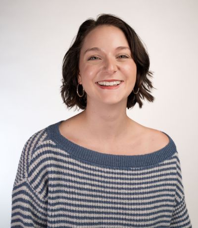 Rylee Spangler A smiling person with short, dark, wavy hair and hoop earrings wears a blue and white striped off-the-shoulder sweater, identified as Rylee Spangler, Systems Analyst Intern. Their favorite product is "Any Bahama Soda!".