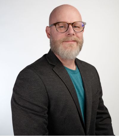Brian Berryhill A smiling man with a bald head, glasses, and a full gray beard wears a dark gray blazer over a teal t-shirt, identified as Brian Berryhill, Director of Finance. His favorite product is Mango with Chili Salt Sno.