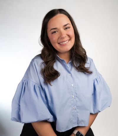 McKaleigh Gustafson A smiling woman with long, dark hair wears a light blue button-up shirt with voluminous sleeves, identified as McKaleigh Gustafson, Finance Manager. Her favorite product is Caribbean Cola.