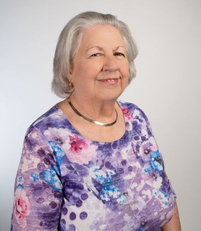 Jewel Parker A smiling older woman with short, gray hair and a gold necklace wears a purple, pink, and blue floral-patterned top, identified as Jewel Parker, Financial Assistant. Her favorite product is Strawberry Cheesecake Sno.