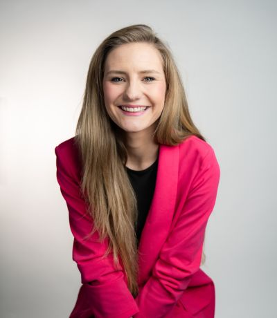 KynnDra Harrison A smiling woman with long, straight blonde hair wears a bright pink blazer over a dark top, identified as KynnDra Harrison, Shop Performance Manager. Her favorite product is Polar Berry Sno.