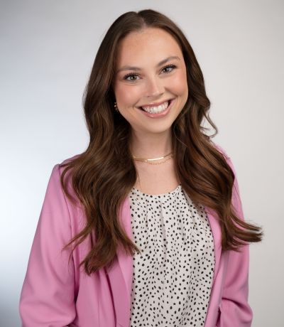 Abby Buchanan A smiling woman with long, wavy brown hair wears a pink blazer over a white top with black polka dots, identified as a Franchise Support Specialist. Her favorite product is Super Sour Watermelon with Chili Salt.
