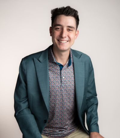 Tru Buchanan A smiling person with dark hair wearing a patterned polo shirt and a teal blazer, identified as Tru Buchanan, Franchise Support Specialist. Their favorite product is Super Sour Watermelon with Chili Salt.