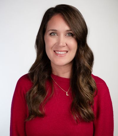Laura Ewing A smiling woman with long, wavy dark brown hair and a gold necklace with an "L" pendant, wearing a red long-sleeved top, identified as Laura Ewing, Executive Support Specialist. Her favorite product is Tropical Blue Coconut Sno.
