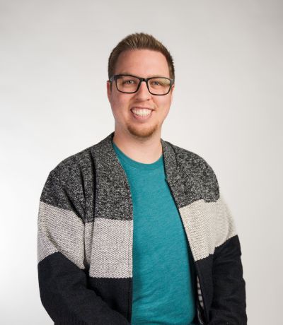 Whalen Garza A smiling person with glasses and short, light brown hair, wearing a teal t-shirt under a black, white, and gray striped cardigan, identified as Whalen Garza, Video Production Specialist. Their favorite product is Kokomoko Island Smoothie.